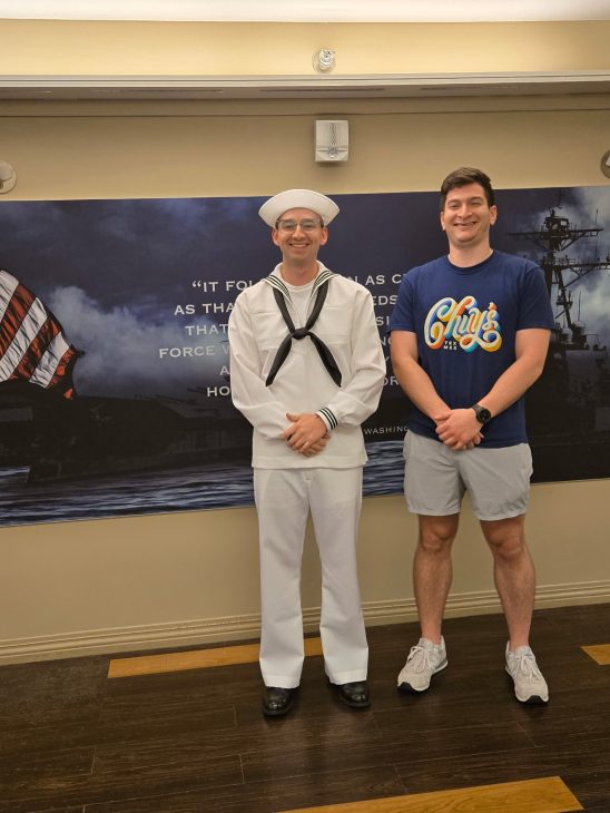 2 men standing in front of a sign at US Navy graduation