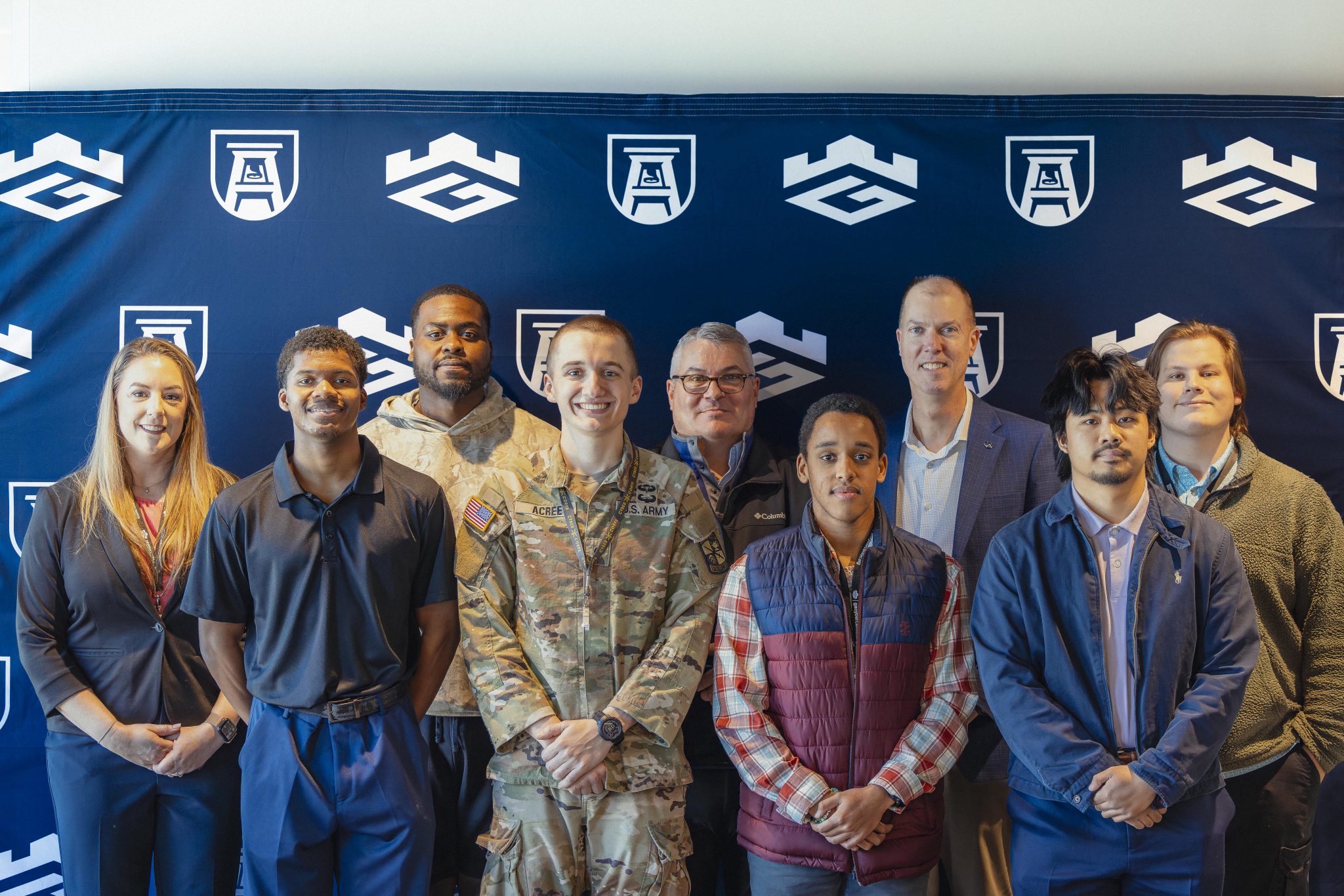Students standing in front of Georgia Cyber Center and Augusta University backdrop, one in military attire