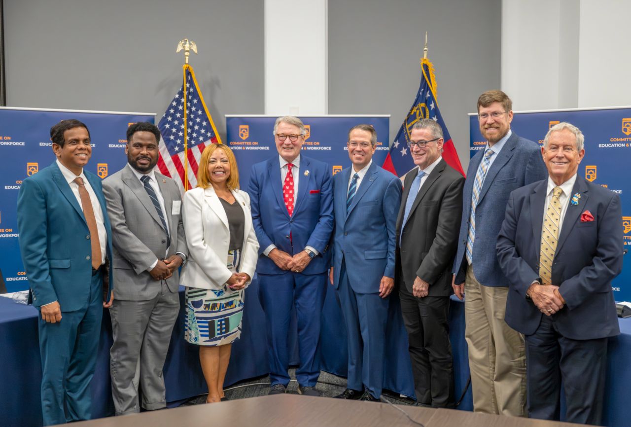 President Russell Keen, Rep. Rick Allen, Joe Wilson, Lucy McBath standing in front of backdrop and flags with witnesses after field hearing at Georgia Cyber Center