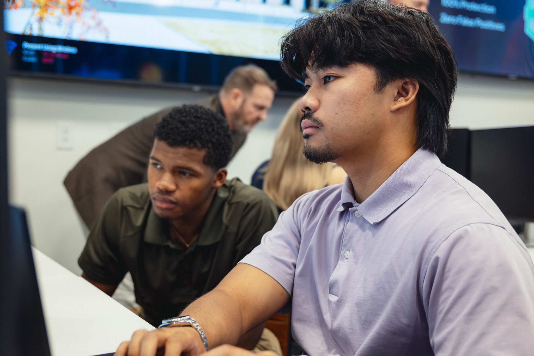 Two focused men sit side-by-side at a desk looking at a computer monitor inside the Cyber Resiliency Center at Augusta University.