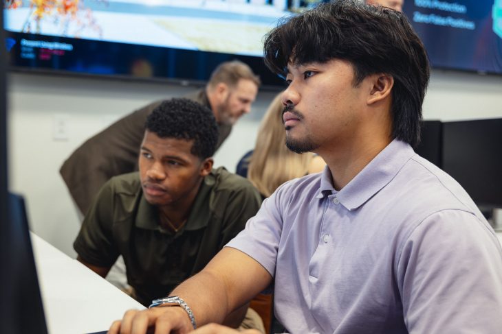 Two focused men sit side-by-side at a desk looking at a computer monitor inside the Cyber Resiliency Center at Augusta University.