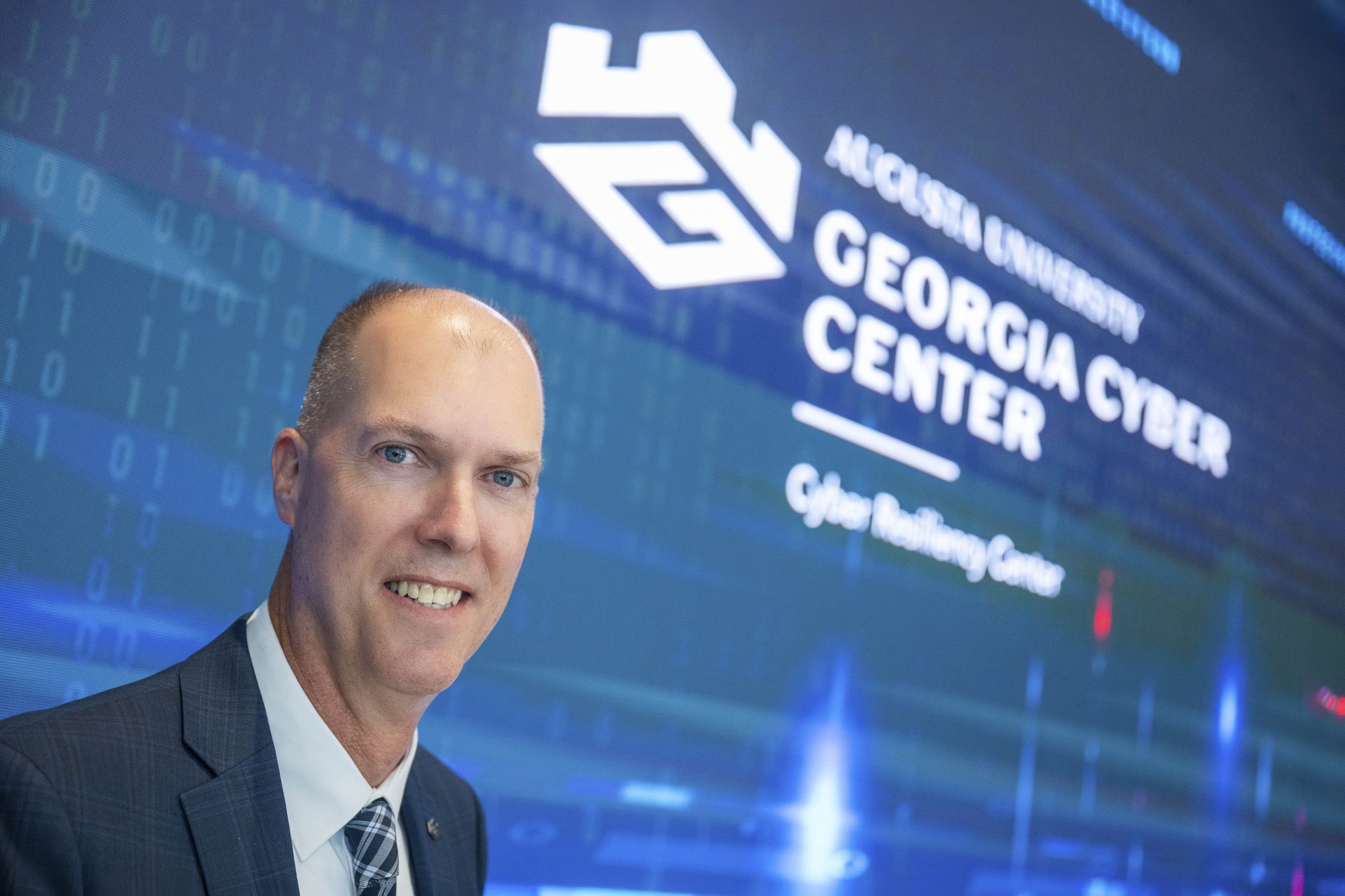 Eric Toler standing in front of large screen with Georgia Cyber Center at Augusta University logo