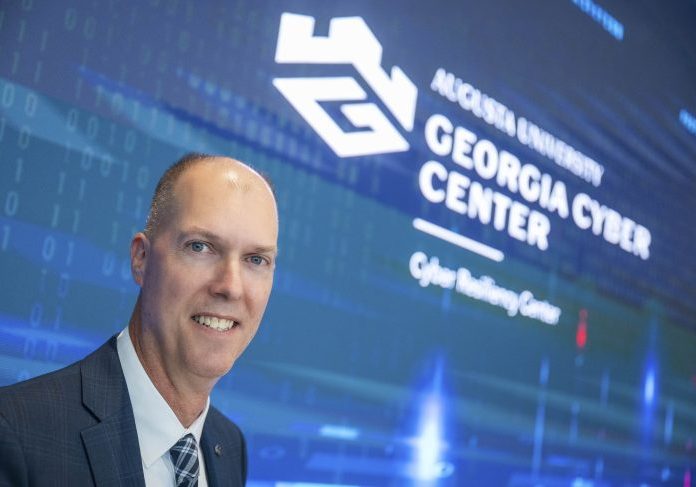 Eric Toler standing in front of large screen with Georgia Cyber Center at Augusta University logo