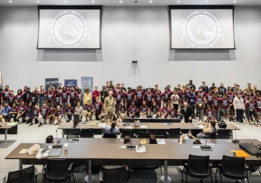 CyberPatriot 2026 Advanced campers stand at the front of the Plug n Play auditorium at the Georgia Cyber Center alongside military officials for graduation ceremony