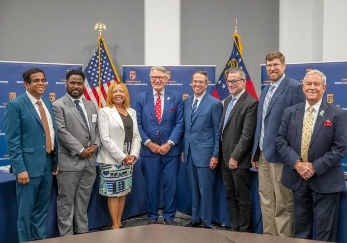 President Russell Keen, Rep. Rick Allen, Joe Wilson, Lucy McBath standing in front of backdrop and flags with witnesses after field hearing at Georgia Cyber Center